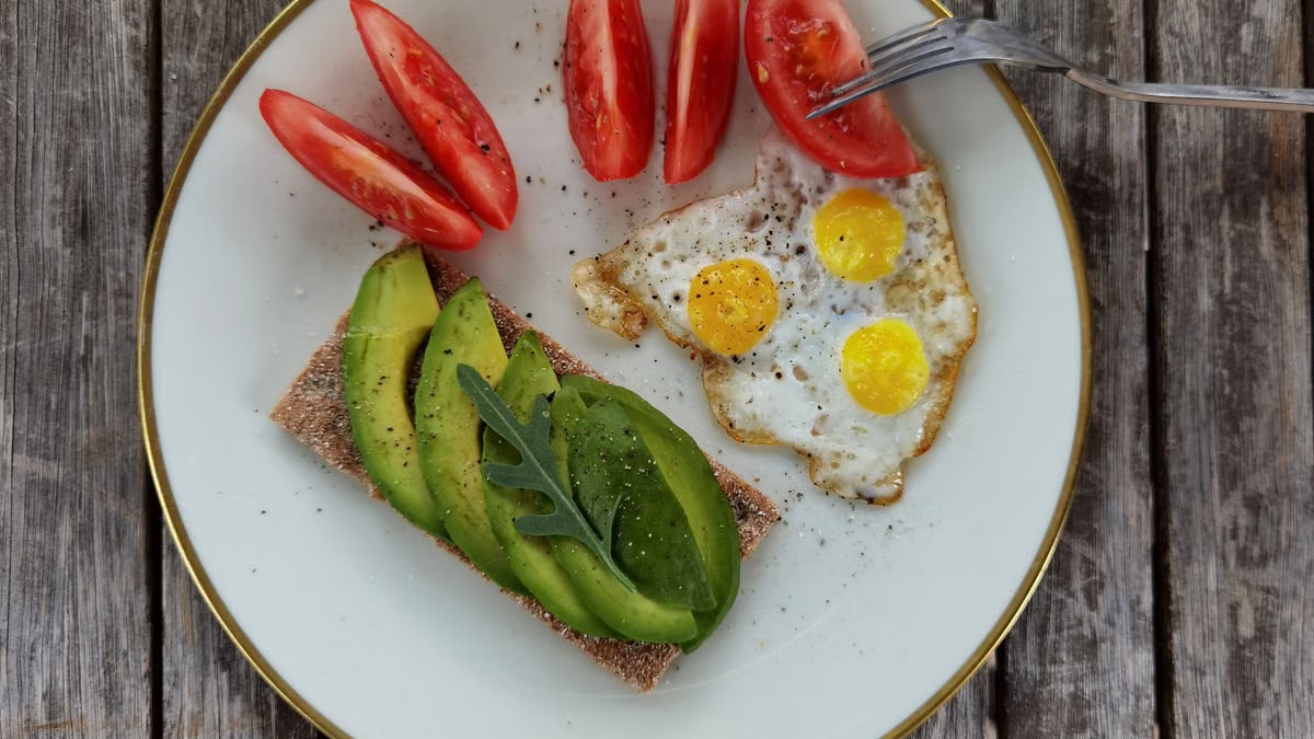 Delicious breakfast plate with sliced avocado, tomatoes, and sunny-side-up quail eggs.